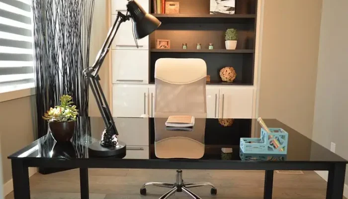 Ein Glas-Schreibtisch mit Tischlampe, Blumentopf und Kalender, begleitet von einem Bürostuhl und einem Regal mit Büchern und Pflanzen, nach einem Büroumzug mit A2B Umzüge.